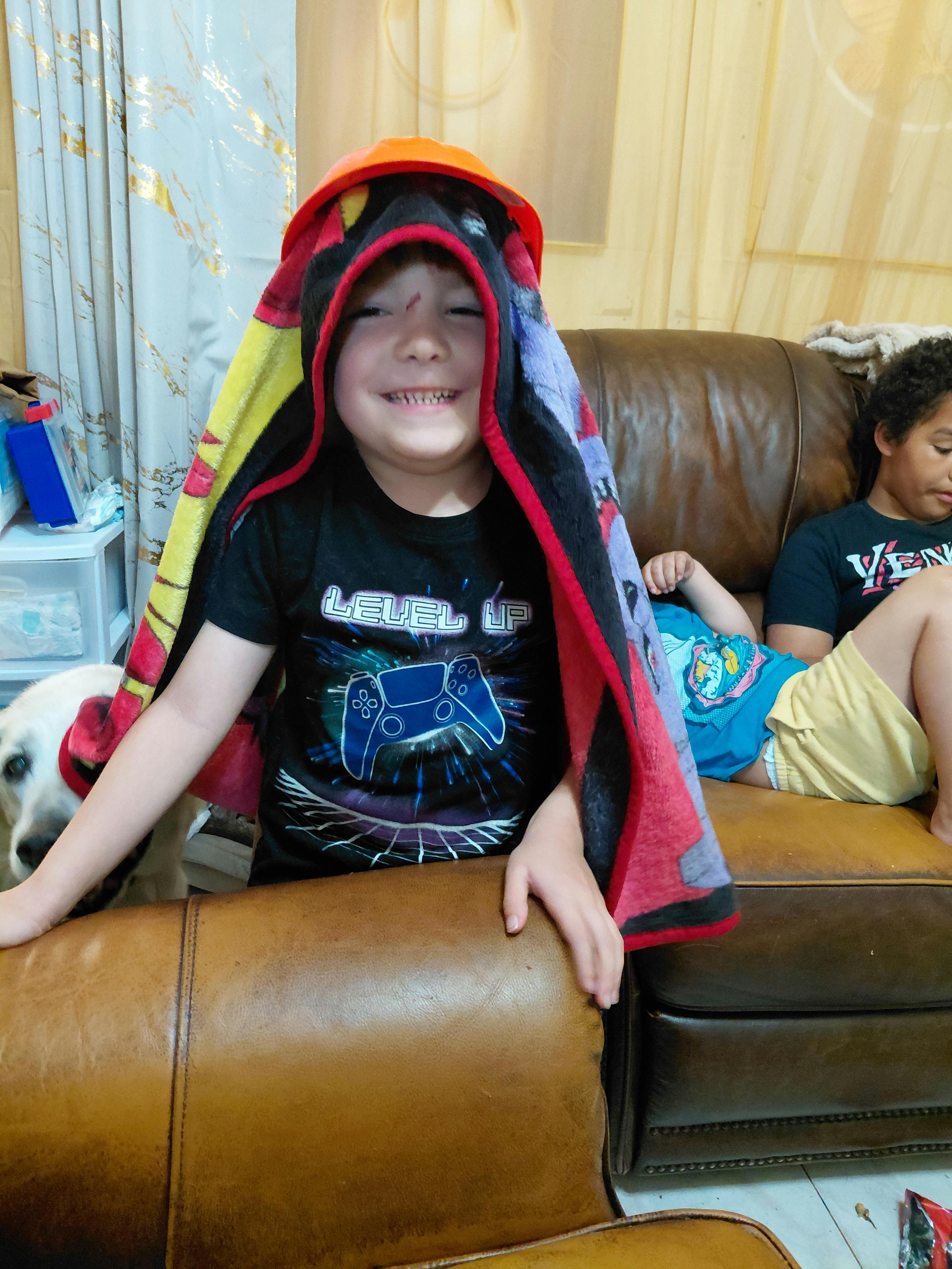Child wearing a hooded blanket on a couch with another child behind