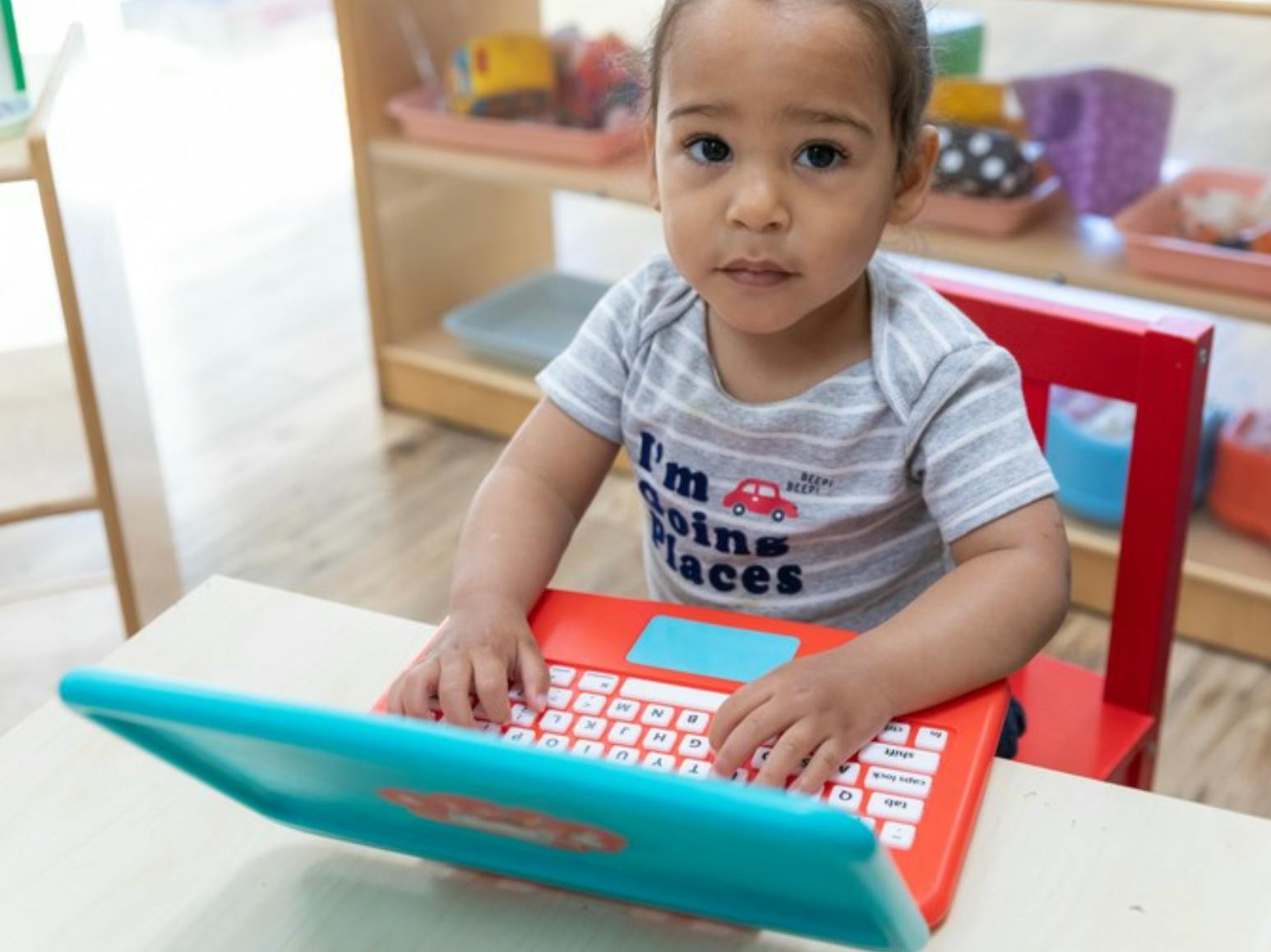 Child looking at camera while playing with a toy laptop