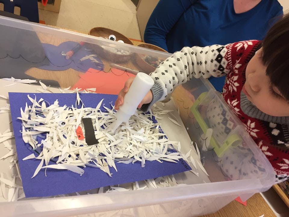 Child applying glue to paper scraps on a table