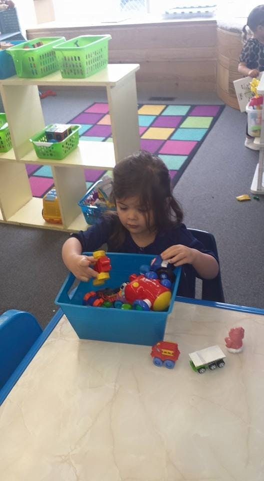 Child playing with toys in a blue bin at a table