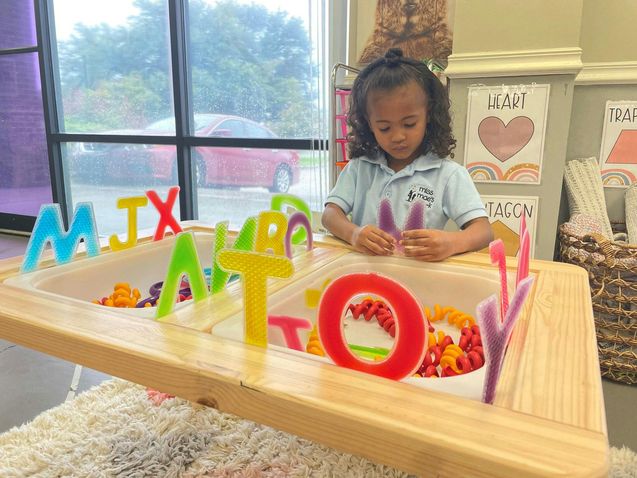 Child playing with colorful letter toys in a sensory table