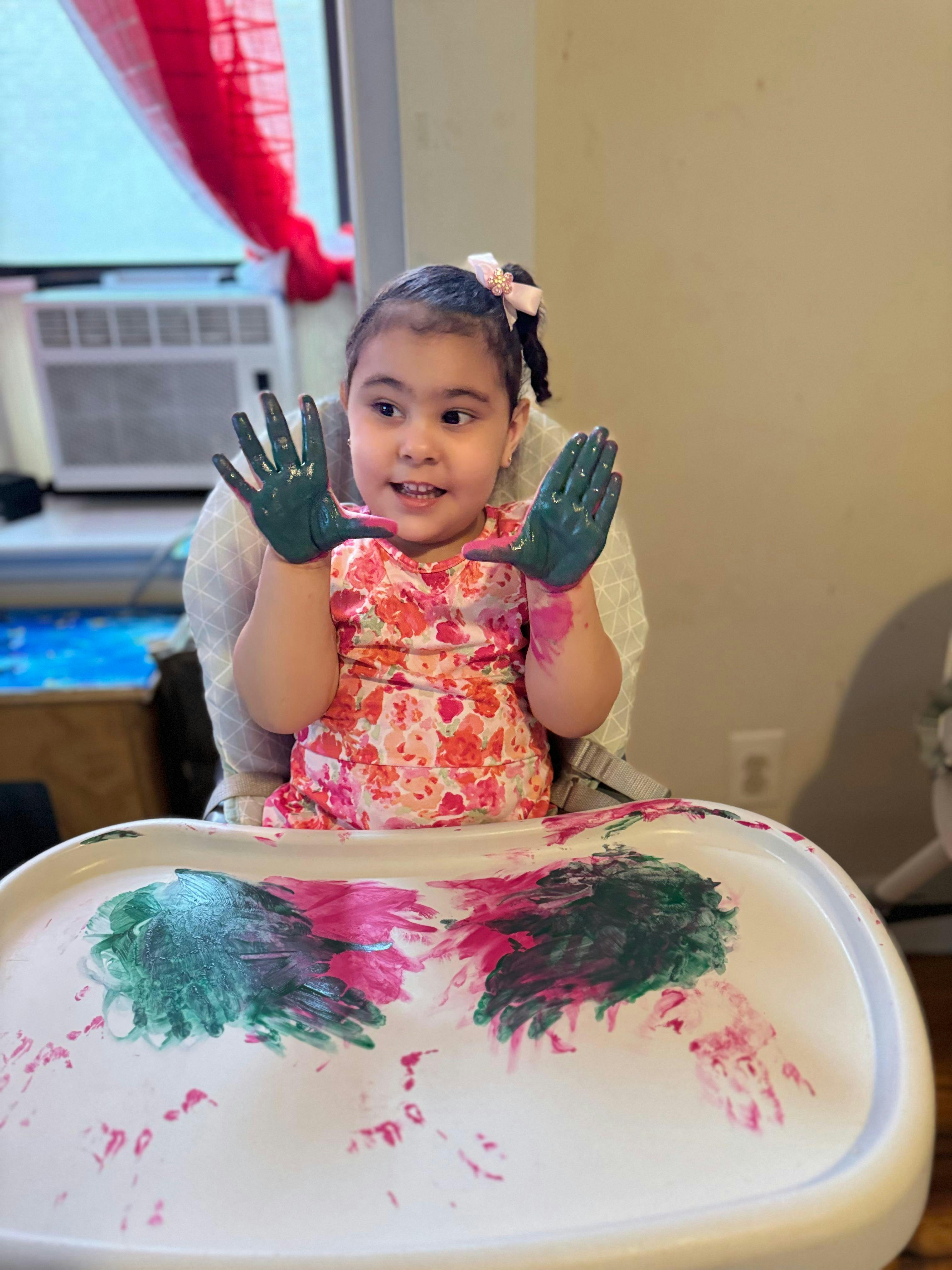 Child in a high chair with paint on hands and the tray