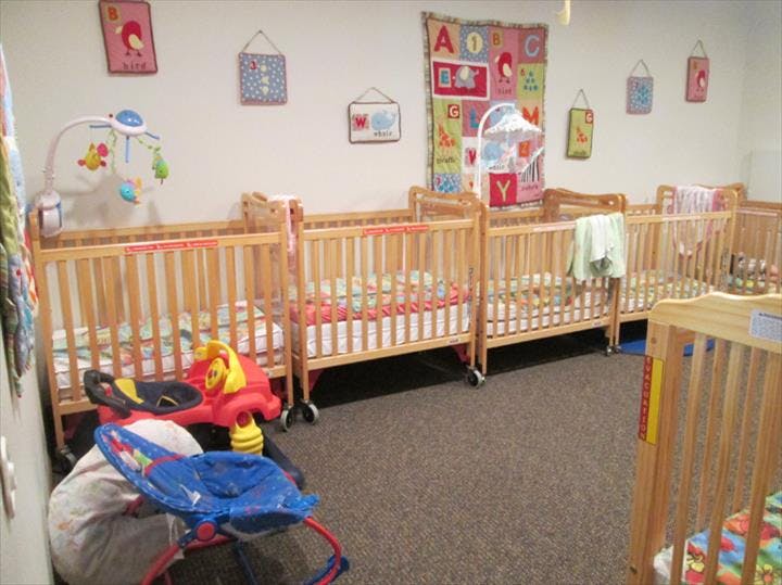 Multiple wooden cribs in a room with toys and wall decorations