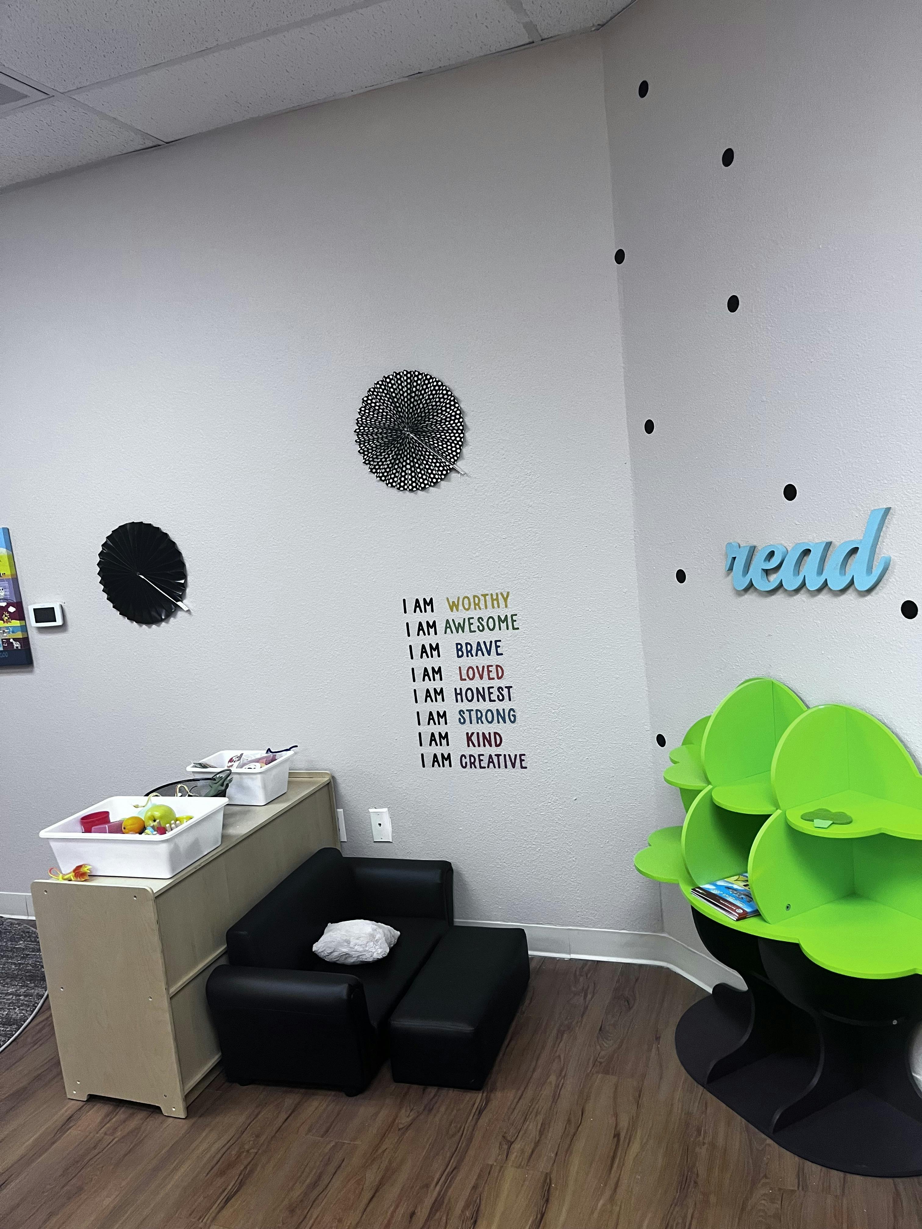 Room with a black chair, green book display, and wall text "I AM WORTHY"