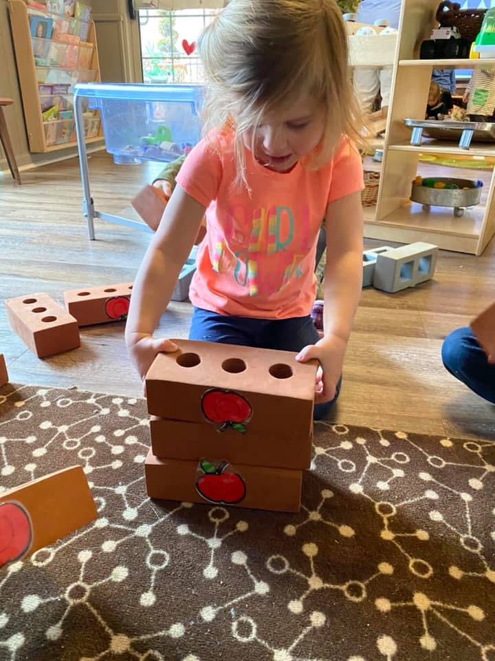 Child stacking toy bricks with apple decals on them