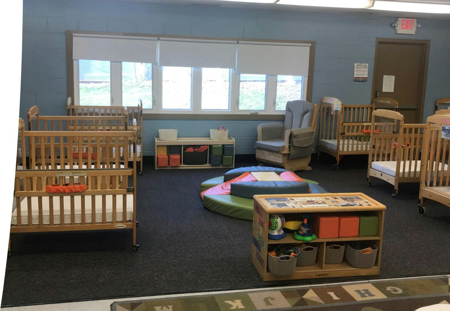 Baby room with several cribs, a rocking chair, and play mats