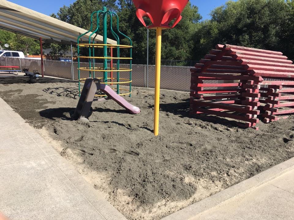 Playground with sand, slide, climbing structure, and red wooden playhouse