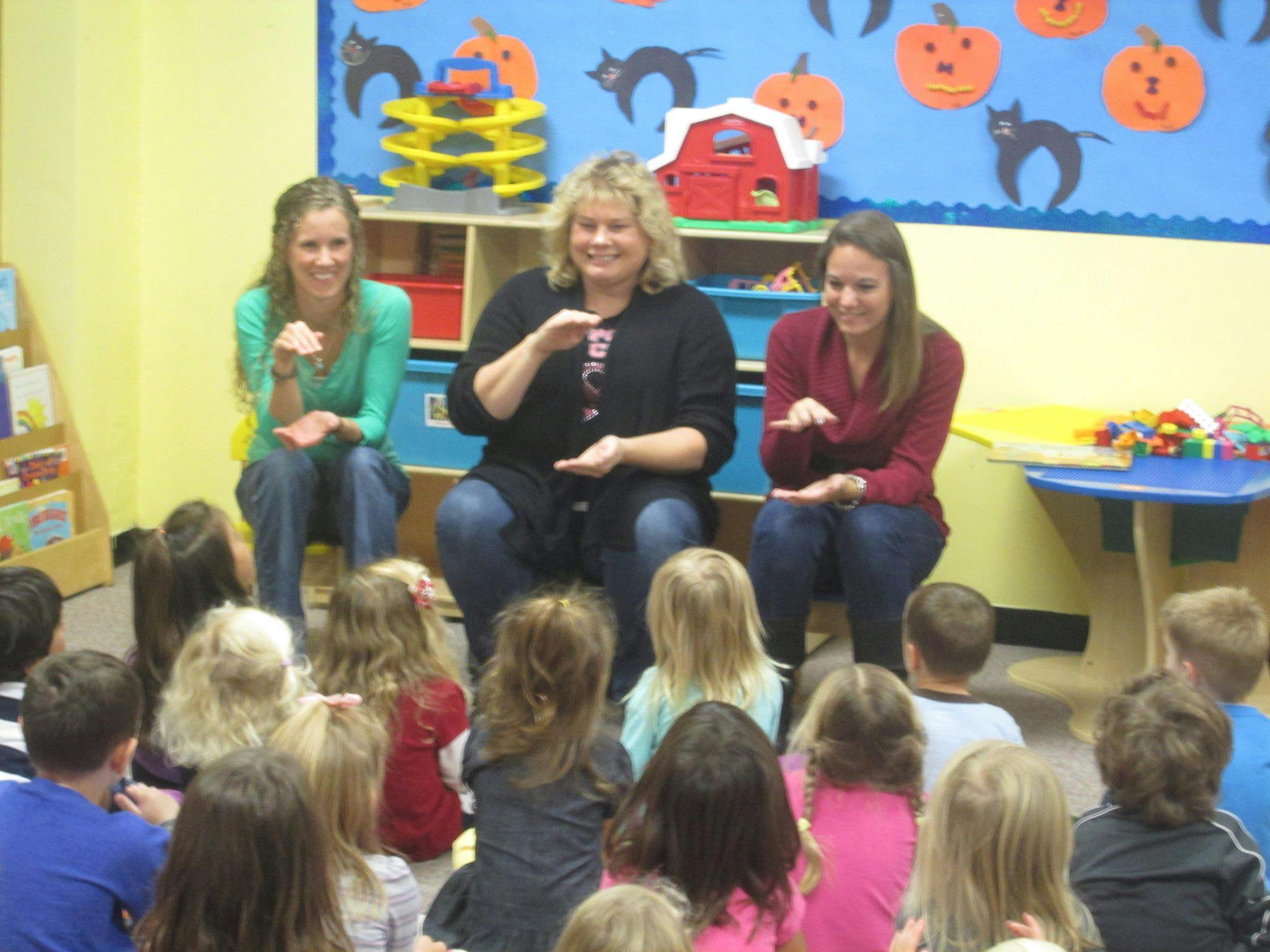 Three people sitting in front of a group of children