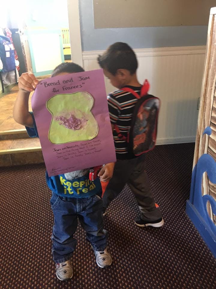 Child holding up a purple paper with a drawing of a peanut butter and jelly sandwich