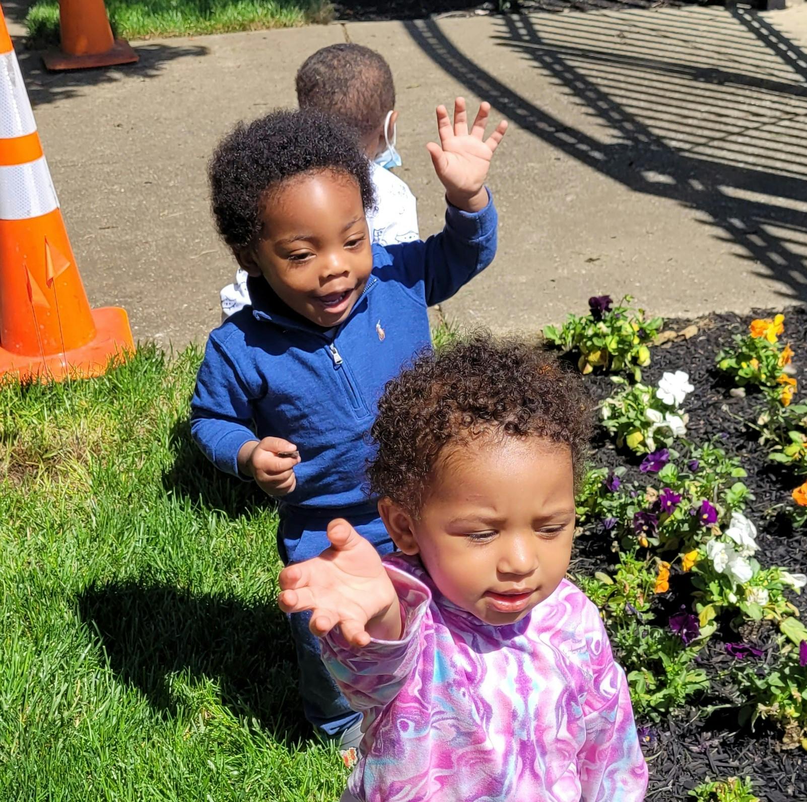 Two children playing outdoors near a flower bed