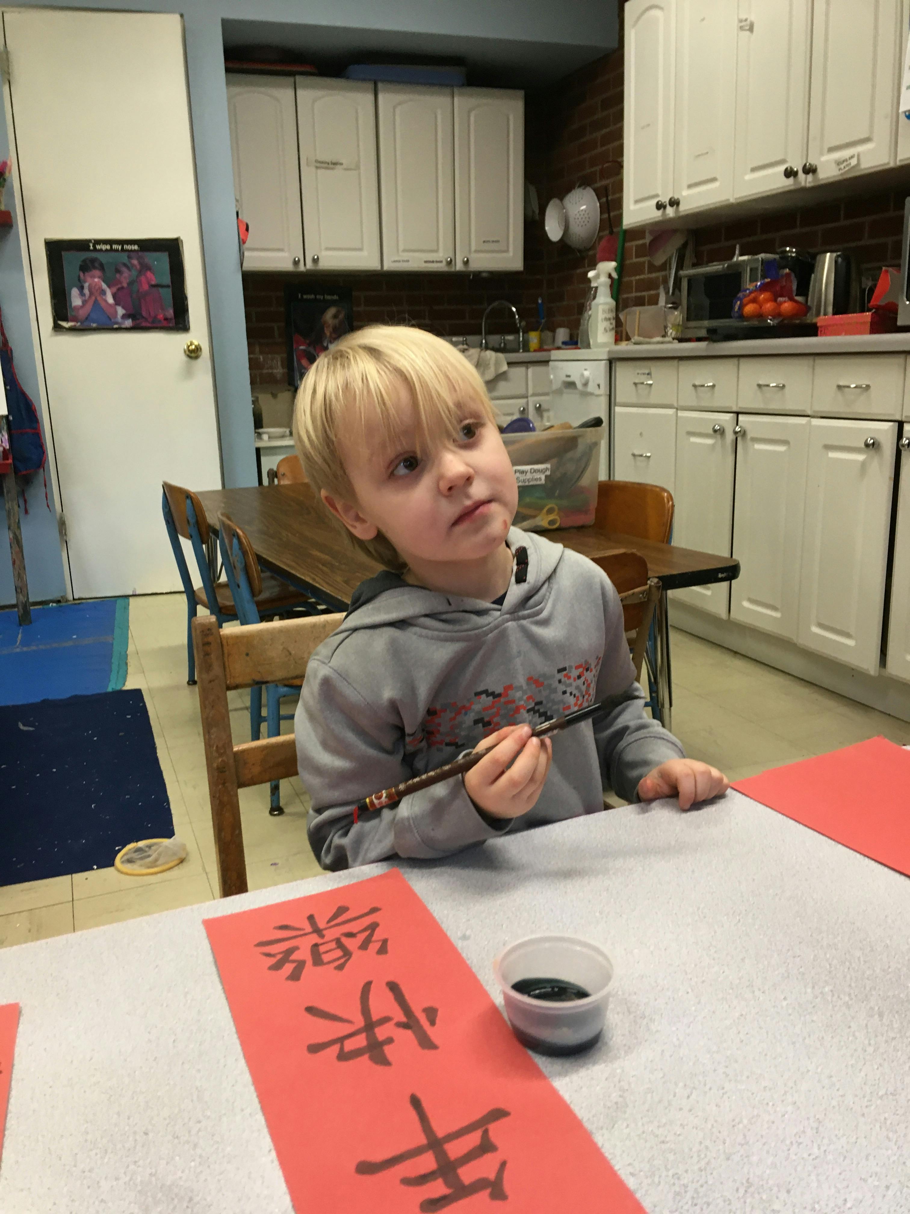 Child holding a paintbrush over red paper with text