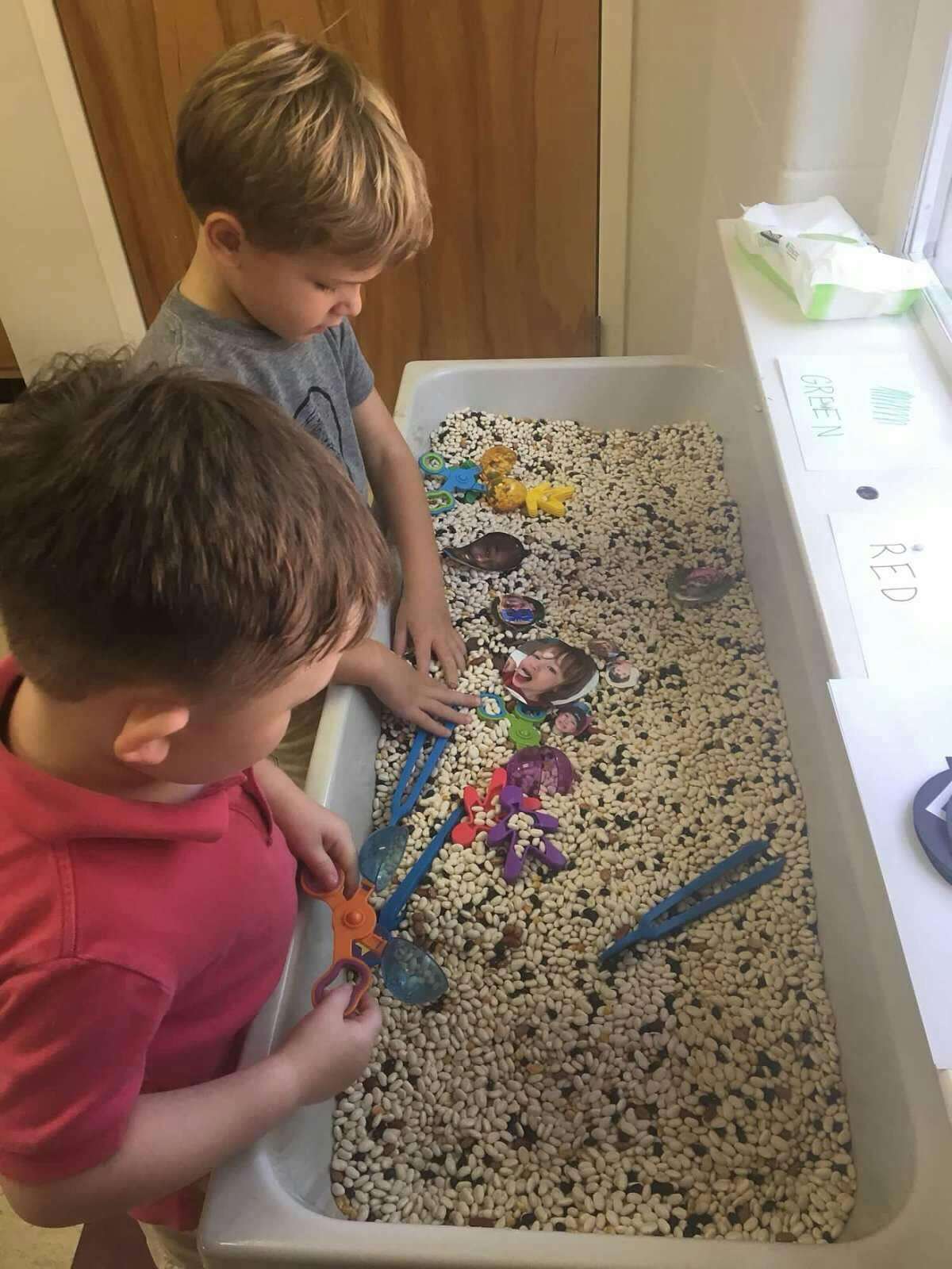 Two children playing with toys in a sensory bin filled with small pellets