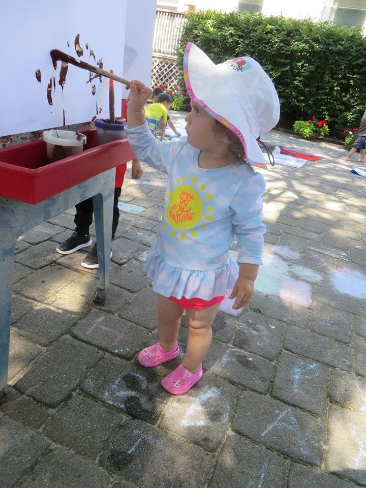 Child in a sun hat painting on a white board outdoors