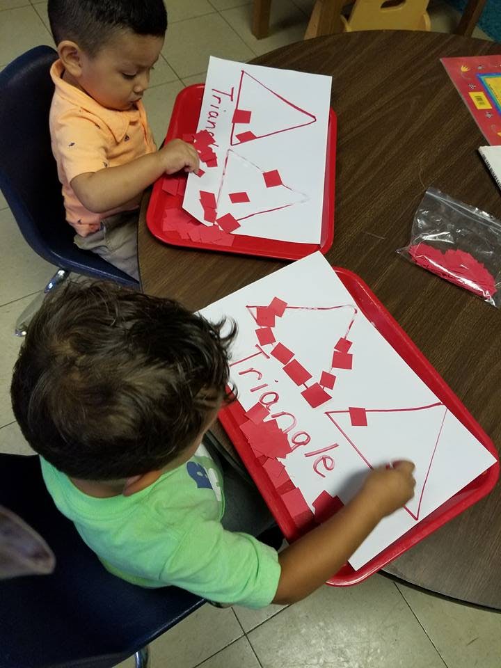 Two children working on triangle-themed crafts at a table