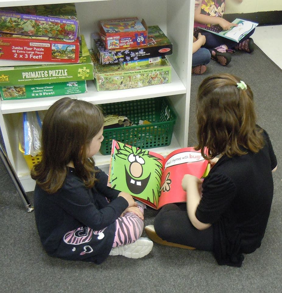 Two children sitting on the floor reading a book together
