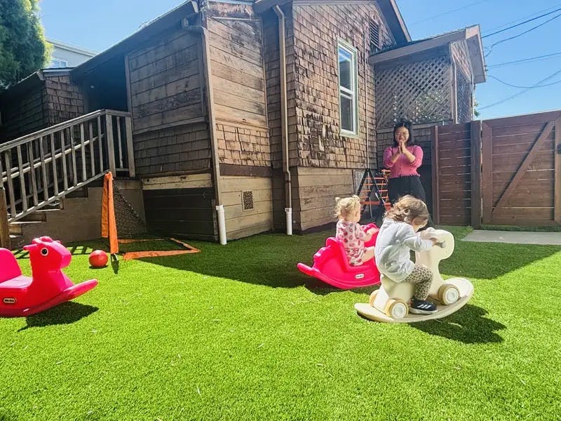 Adult watching two children playing on rocking horses on grass