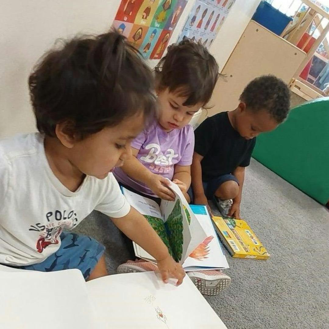 Three children looking at books on the floor in a classroom