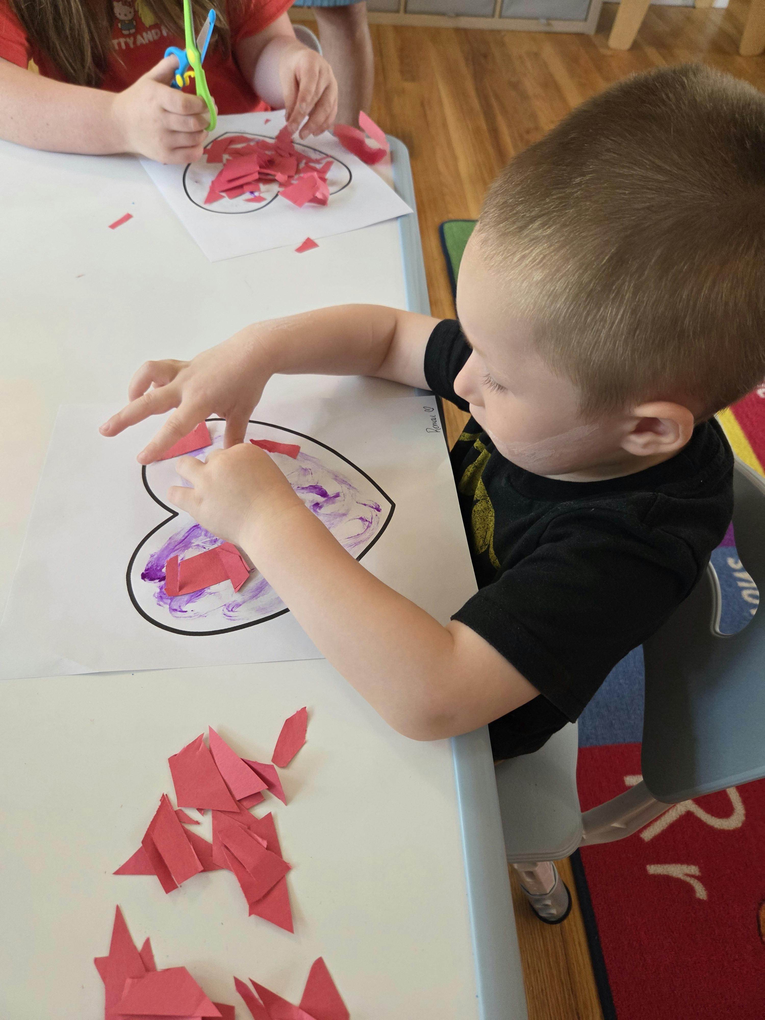 Child gluing paper pieces onto a heart cutout at a table