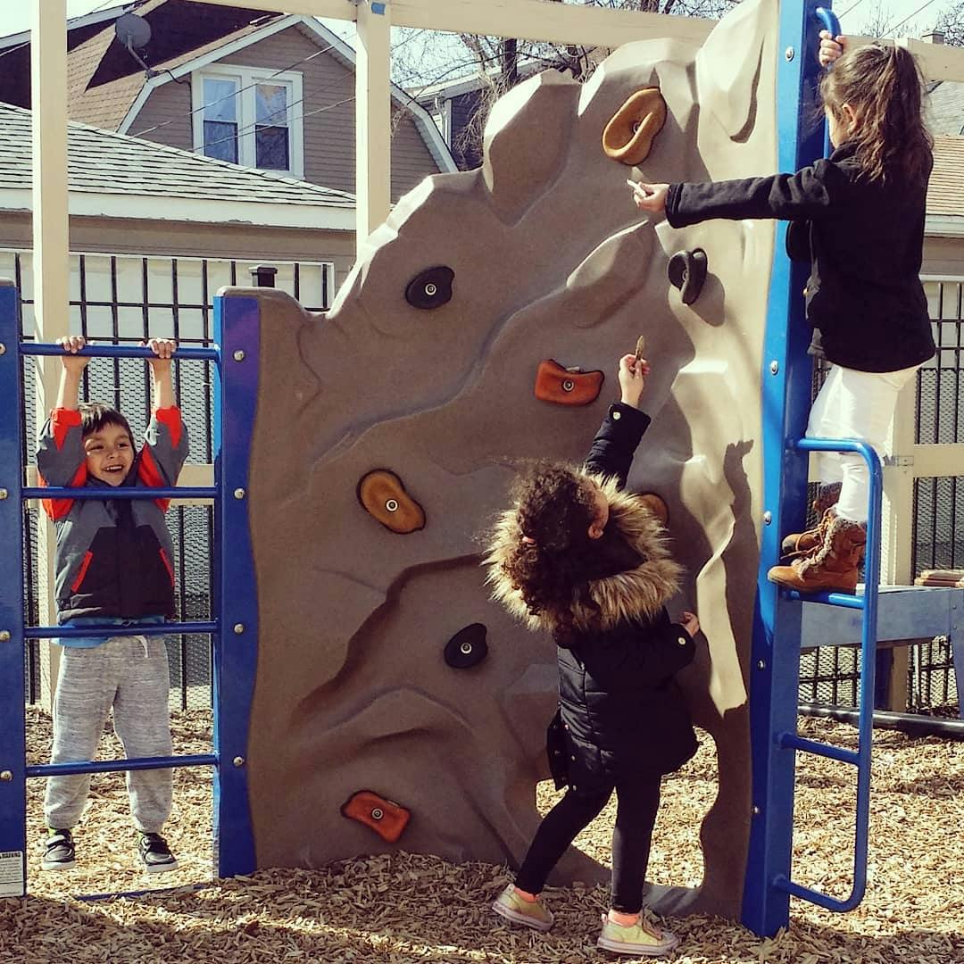 Three children playing on a rock climbing wall and playground