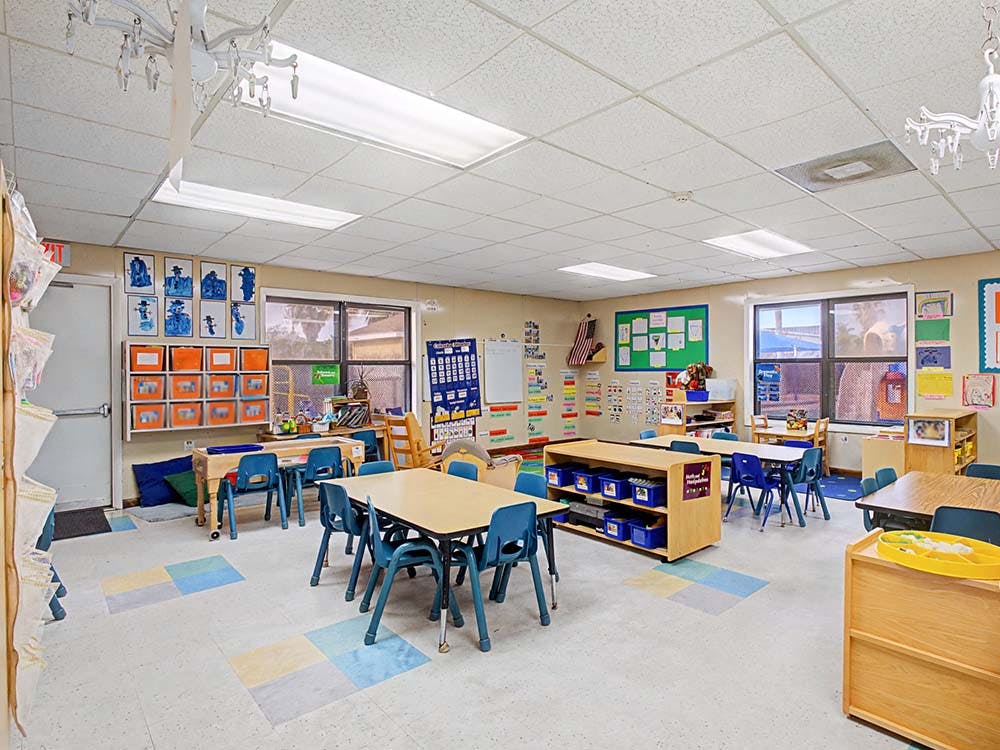 Empty classroom with small tables and chairs, and student artwork on the wall