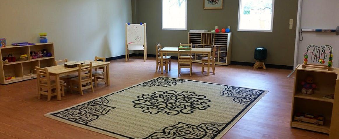 Classroom with small wooden tables and chairs, shelves, and a patterned rug