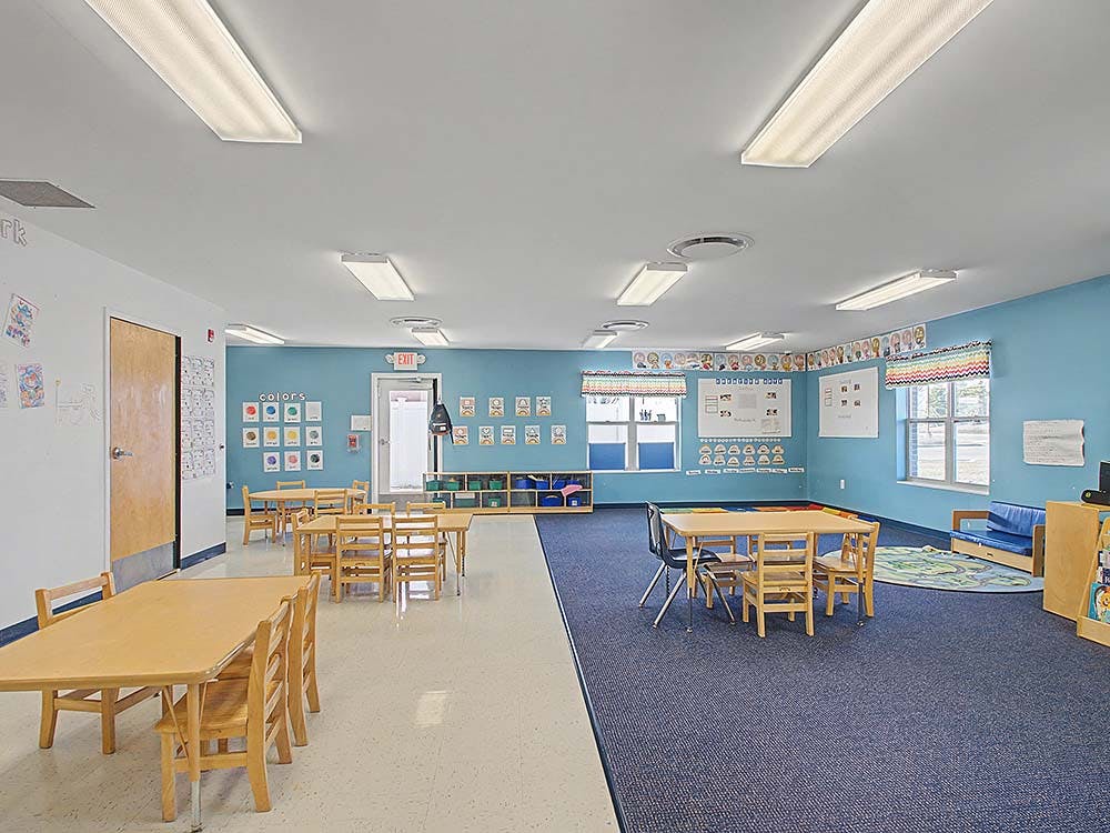 An empty classroom with small tables and chairs, half carpet, half tile