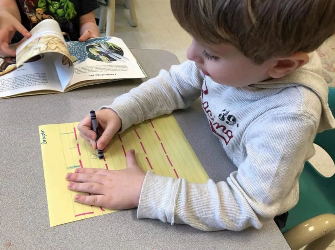Child writing on yellow paper with a marker