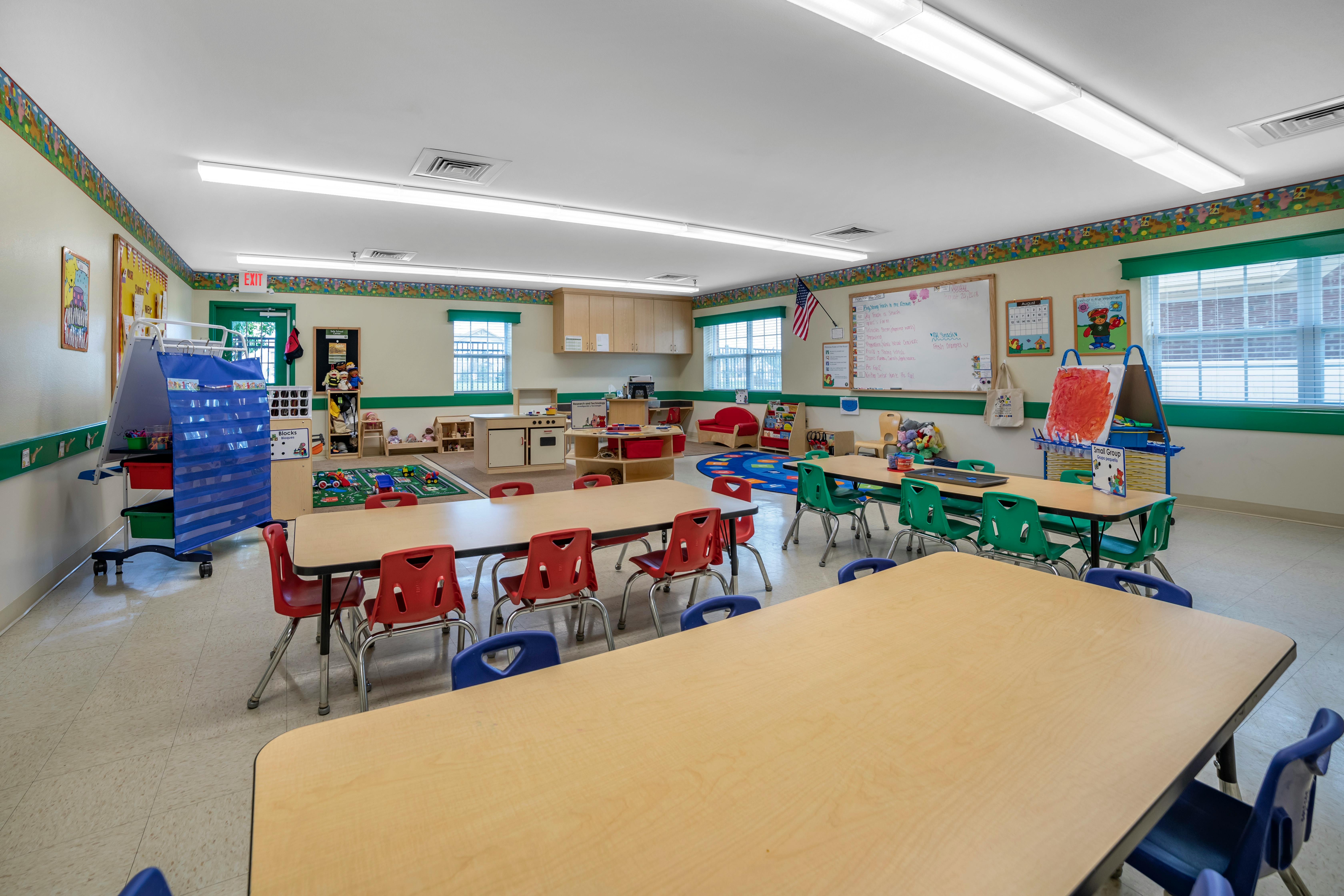 Empty classroom with small tables and chairs, toys, and learning materials