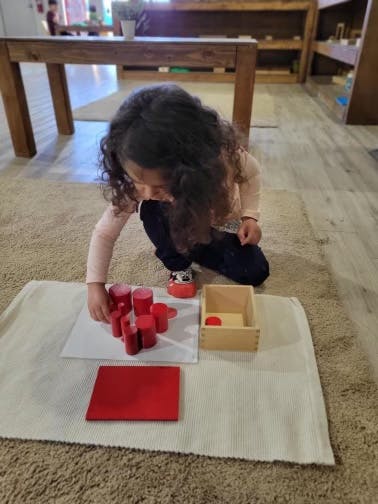 Child playing with red cylindrical blocks on a mat