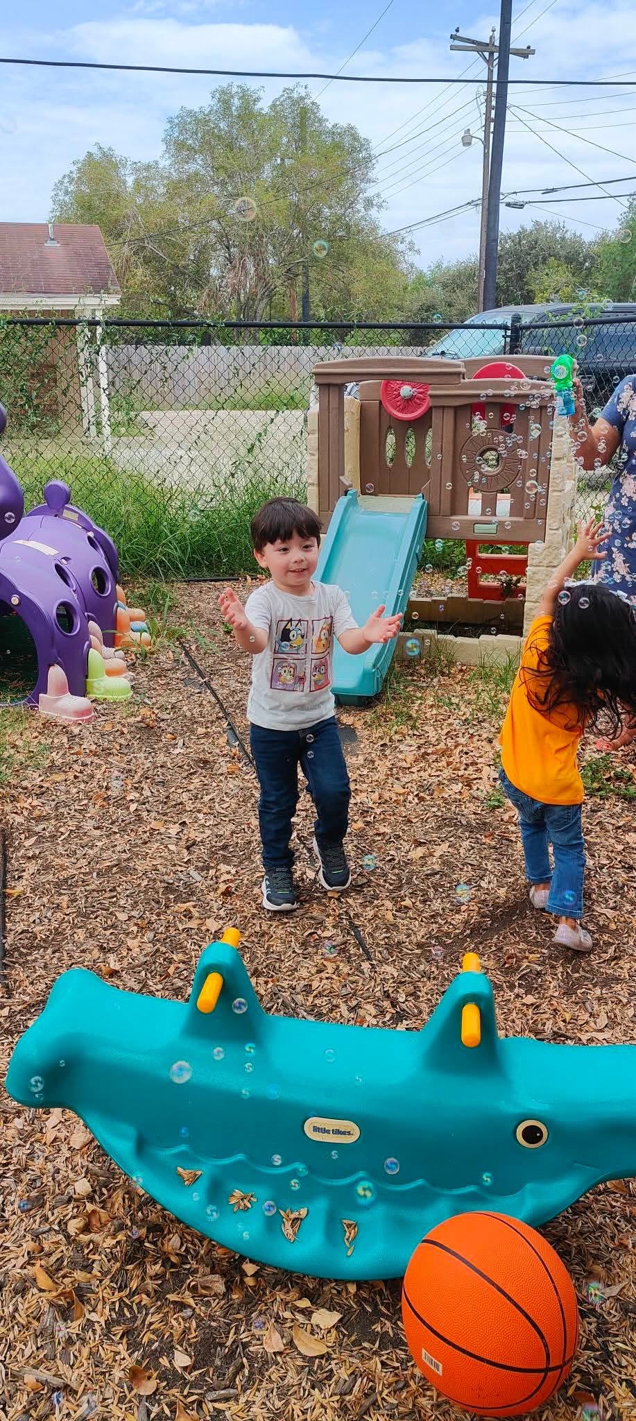 Two children playing with bubbles outdoors near a slide and playground equipment