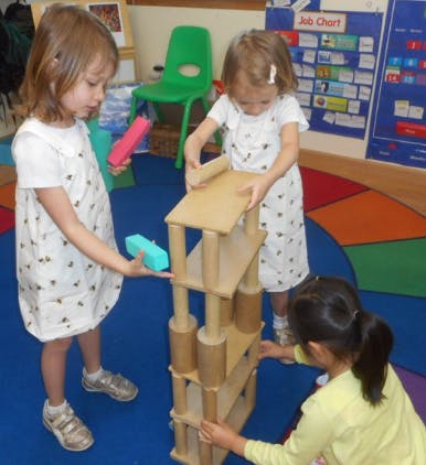 Three children building a tall structure with wooden blocks