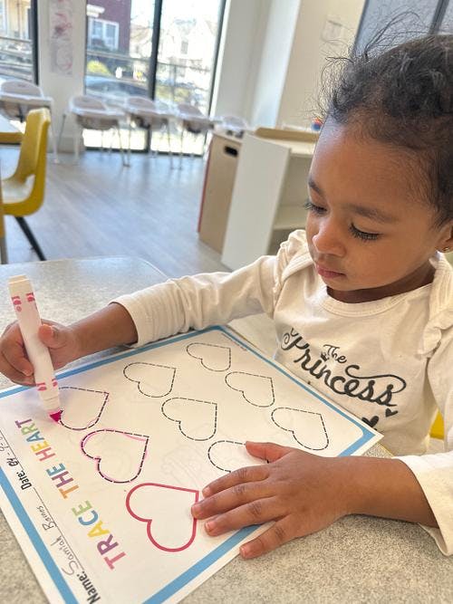 Child tracing heart shapes on a worksheet with a marker