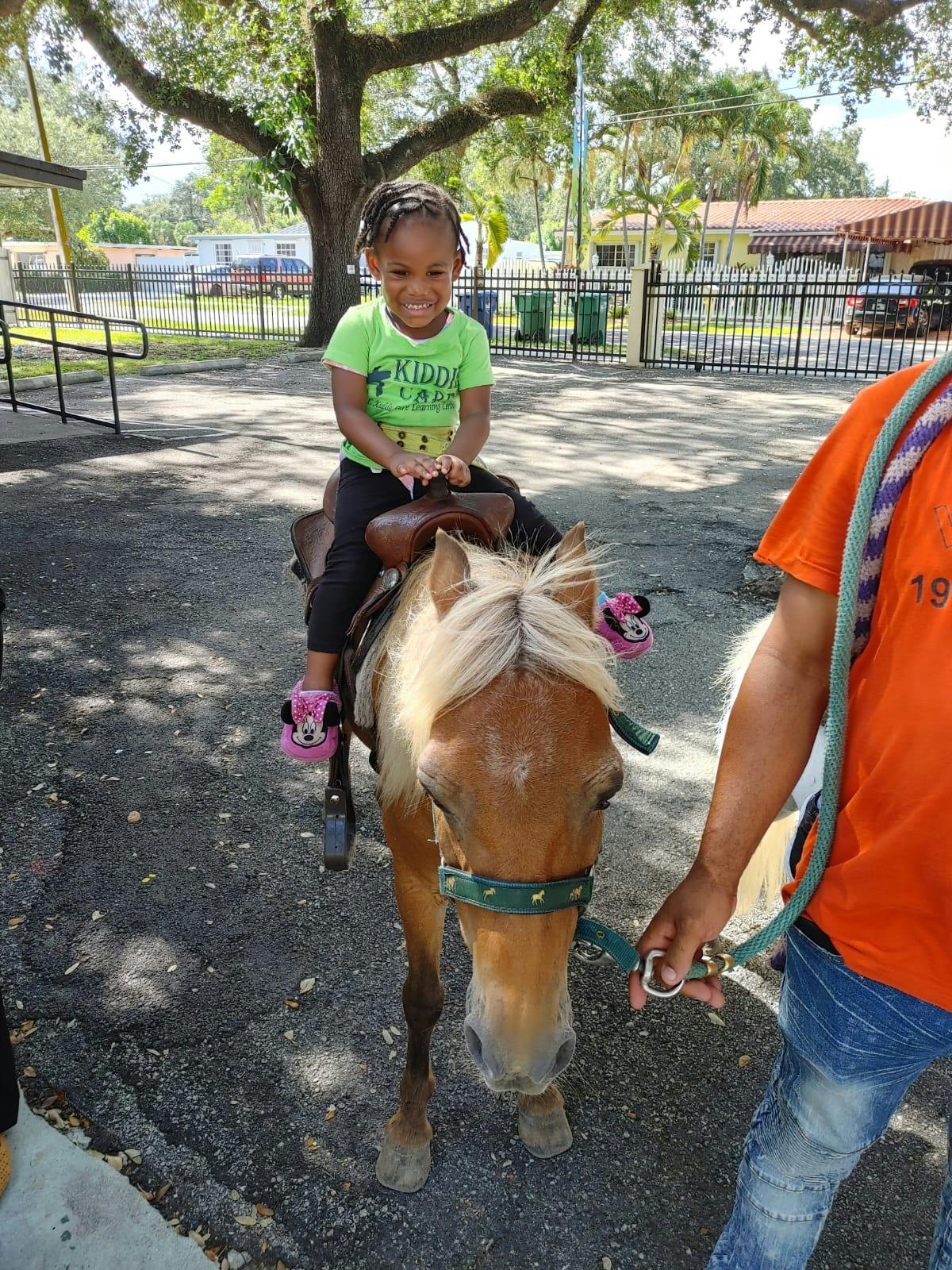Child riding a pony led by a person
