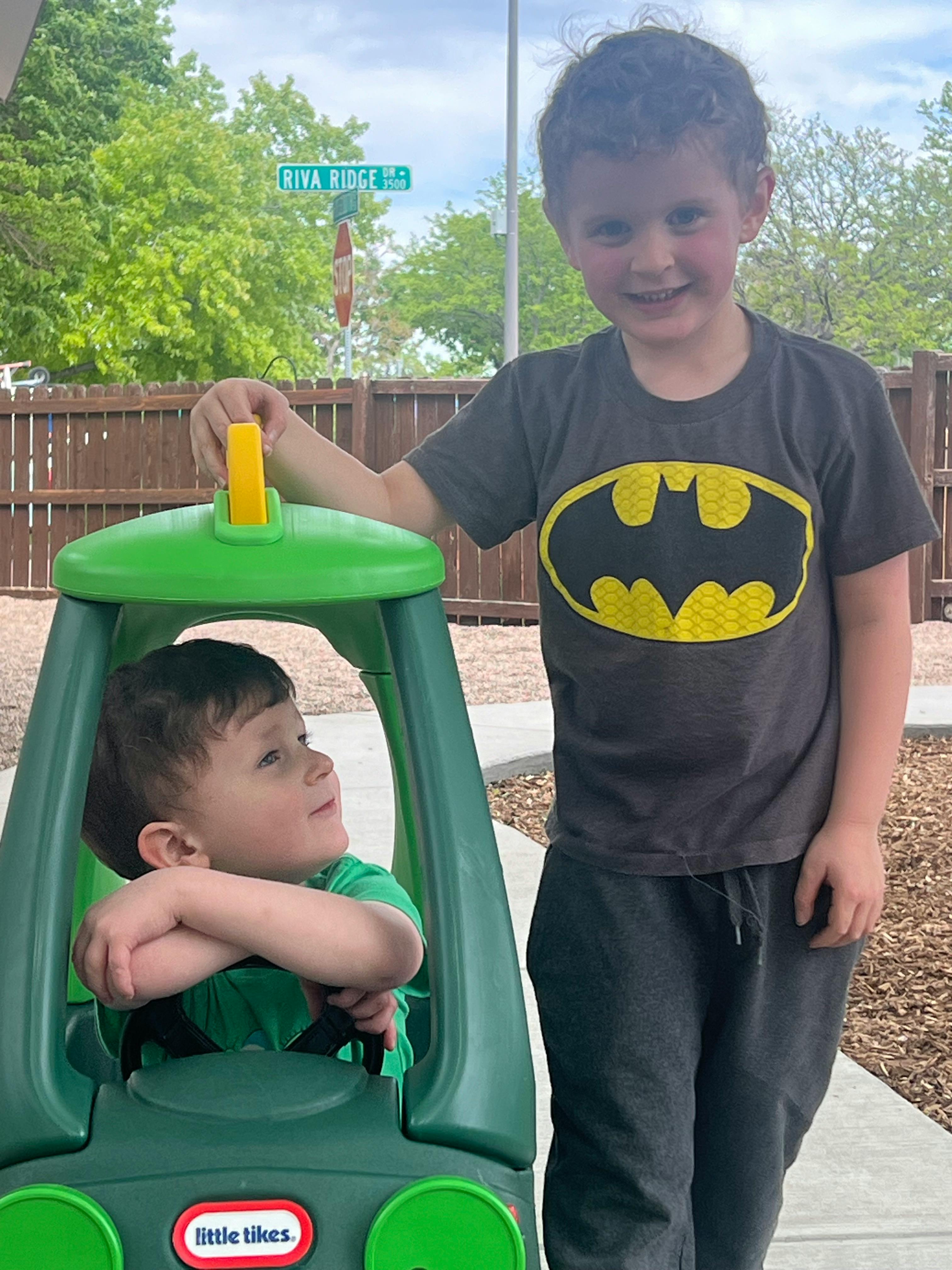 Child in a green toy car with another child standing beside it