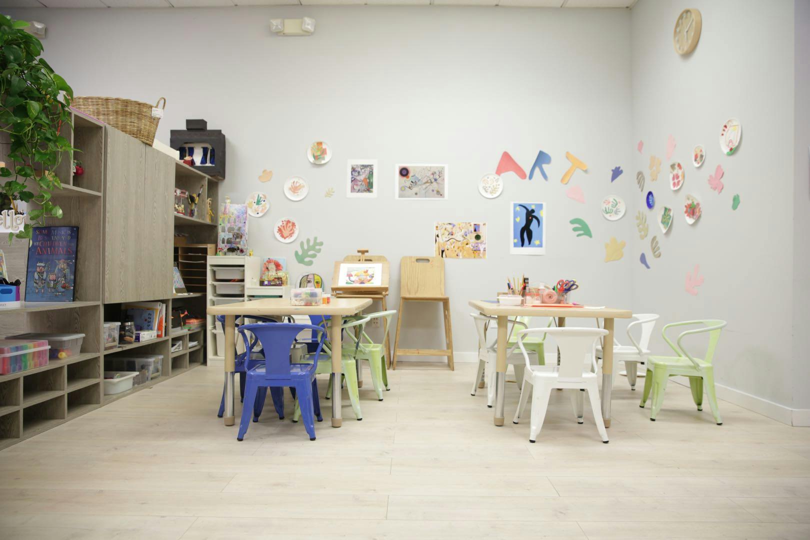 Classroom with small tables and chairs, artwork on the wall