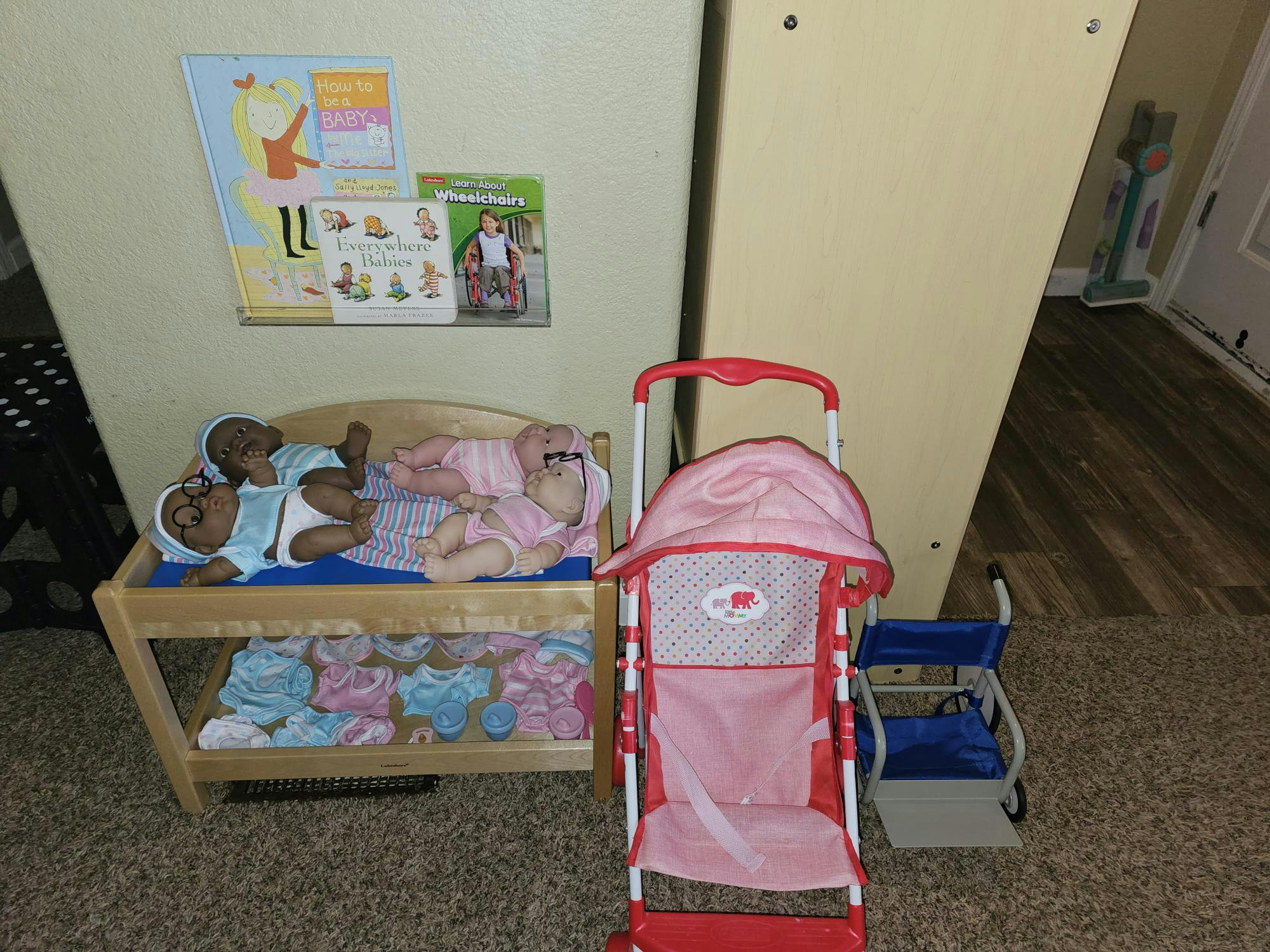 Doll changing table with baby dolls next to a toy stroller and wheelchair