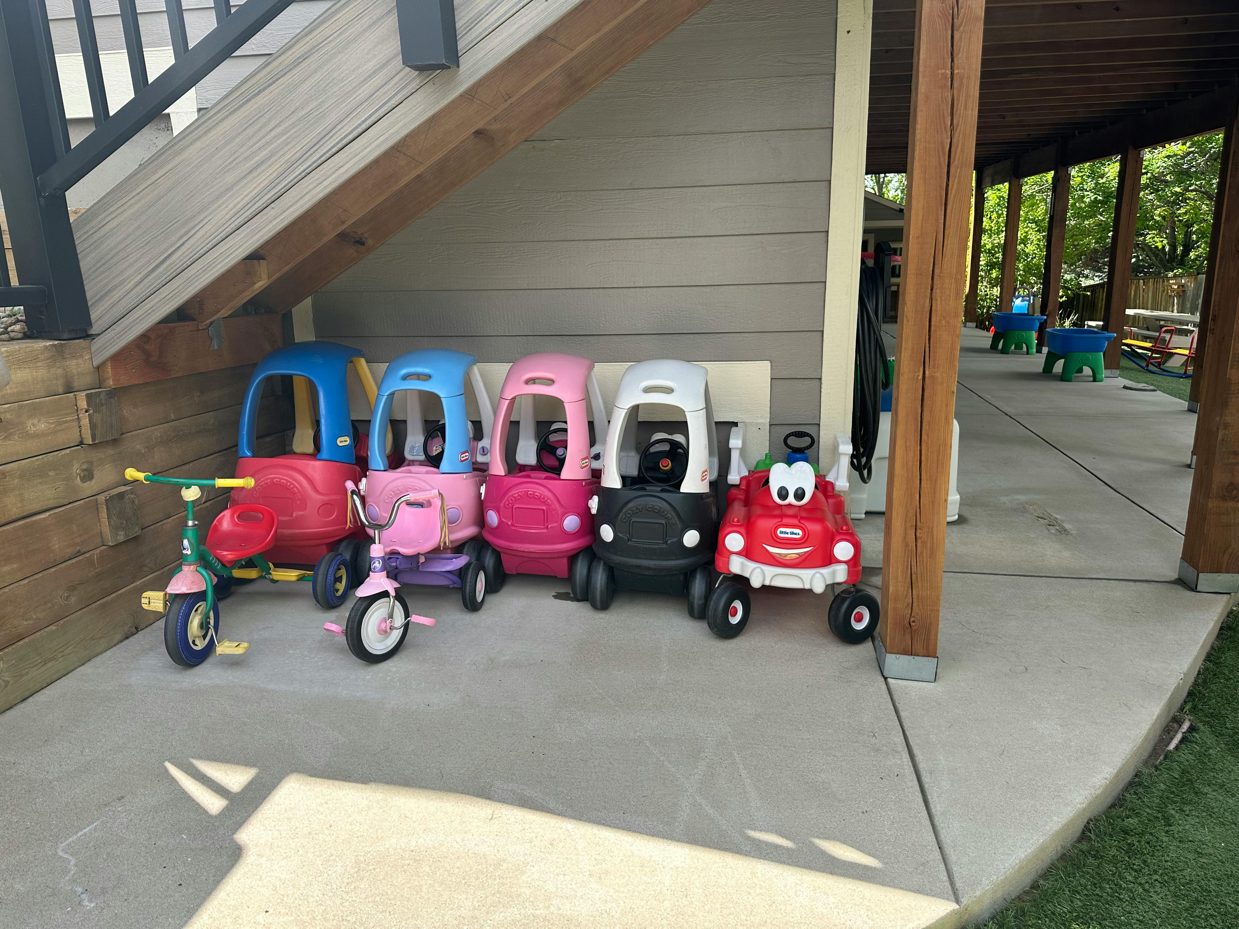 Children's ride-on toys and tricycles lined up under an overhang