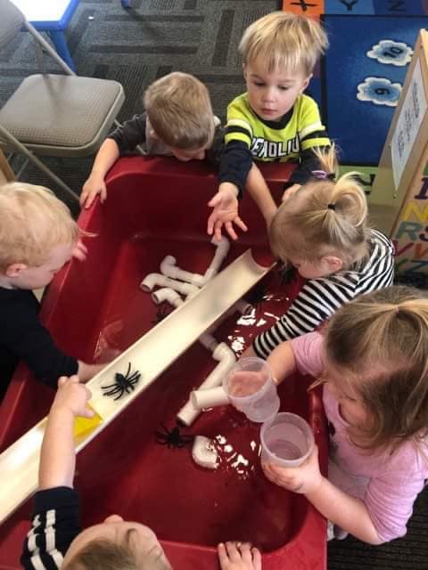 Children playing with water and pipes in a red bin