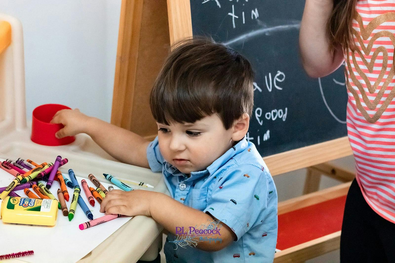 Child reaching for crayons on a table