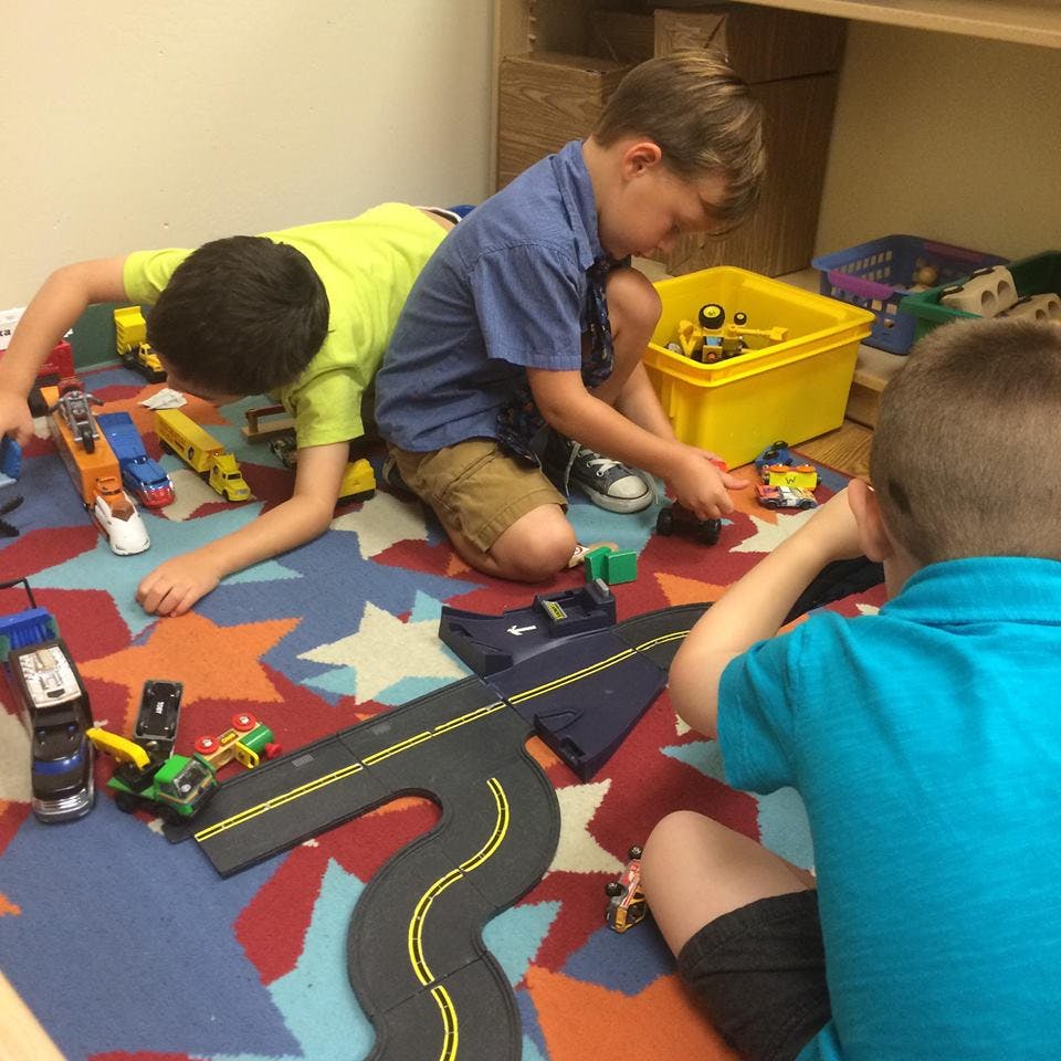 Three children playing with toy cars and a road mat on a patterned rug