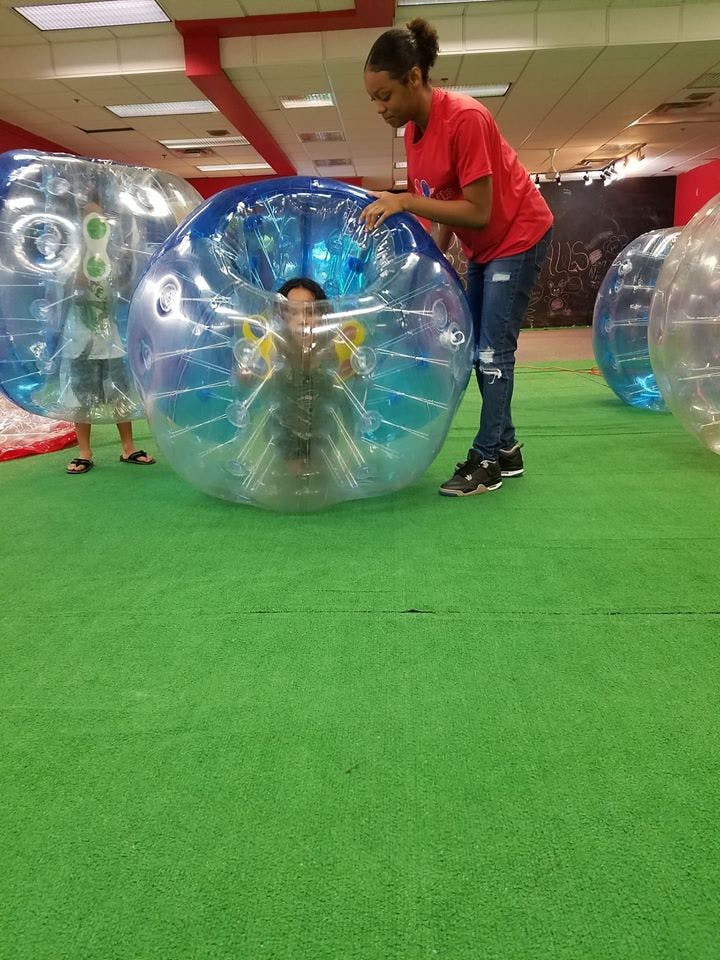 Person helping a child in a large inflatable bubble on a green floor