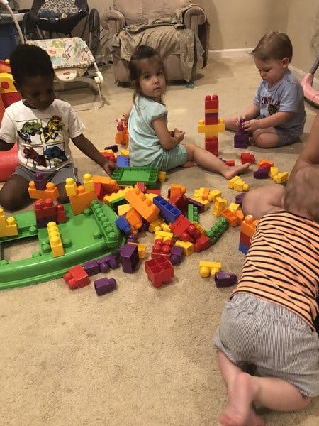 Three children playing with colorful building blocks on a carpeted floor