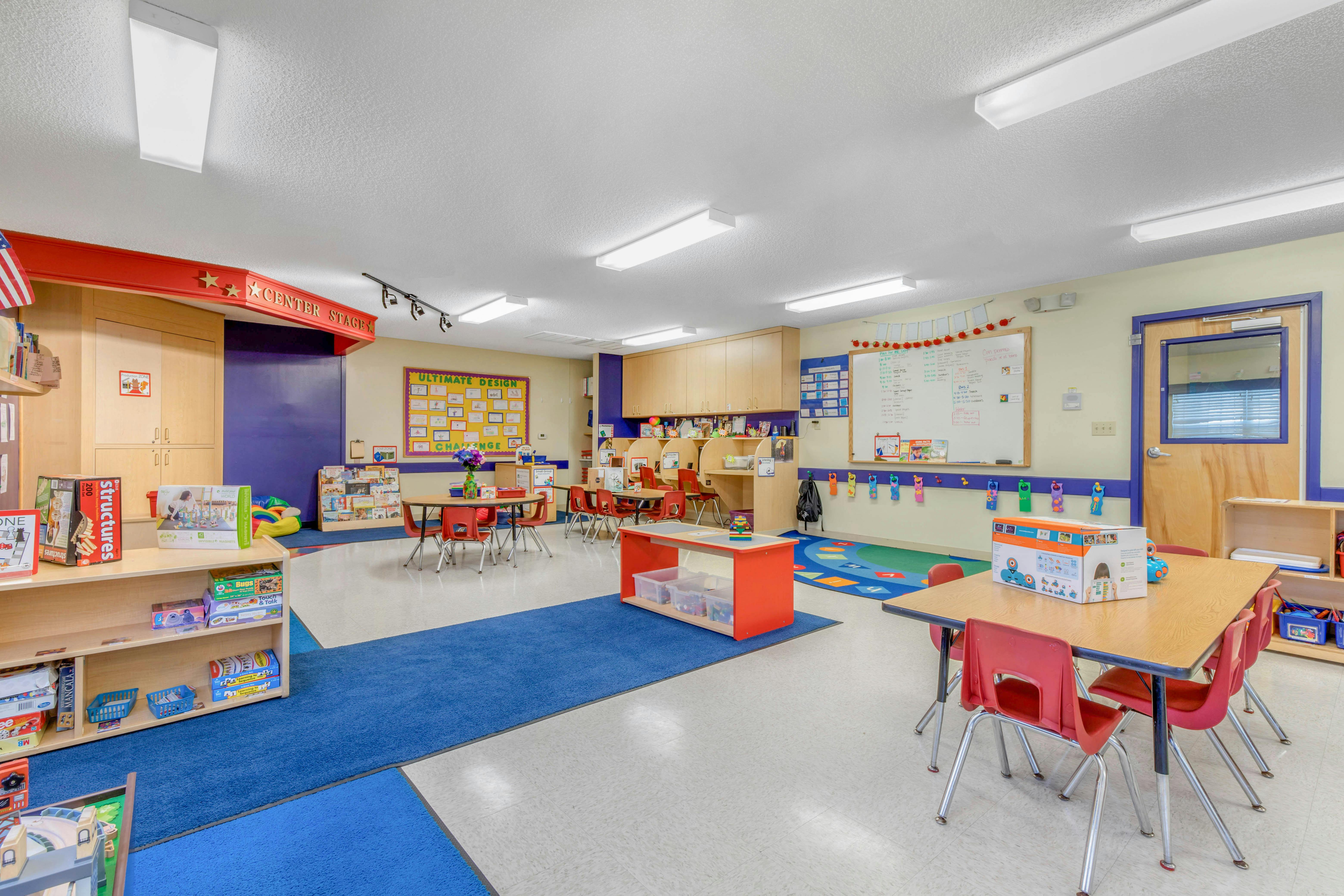 Classroom with multiple tables and chairs, play mats, and learning materials
