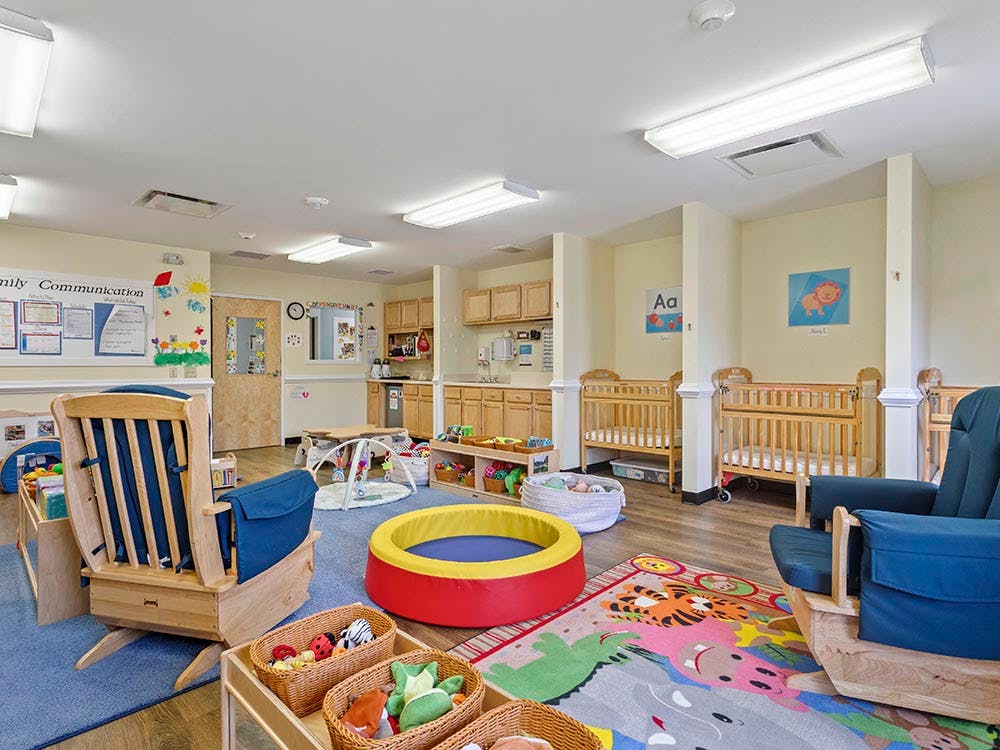 A colorful childcare room with cribs, rocking chairs, and toys