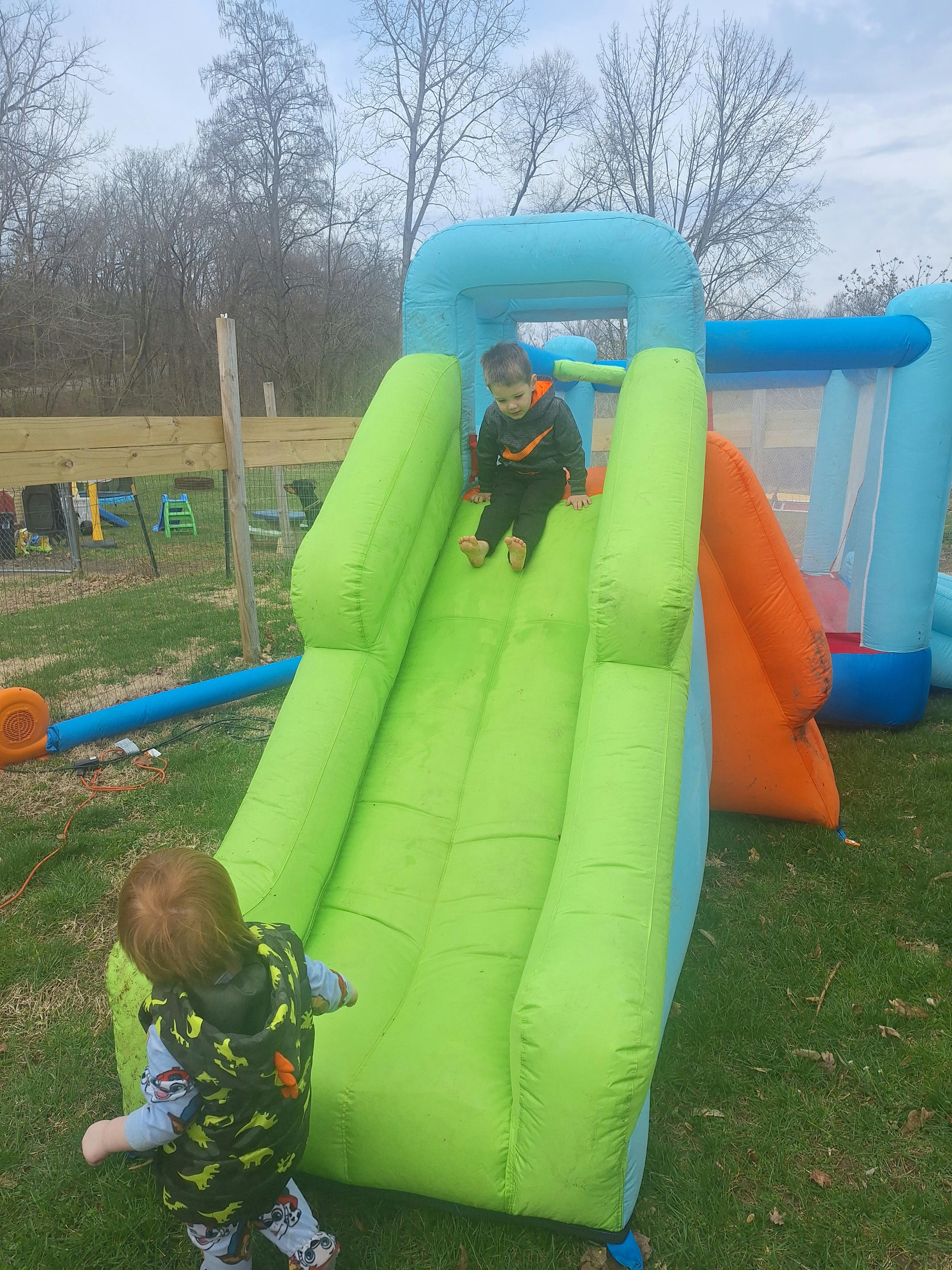 Child on a green inflatable slide with another child nearby