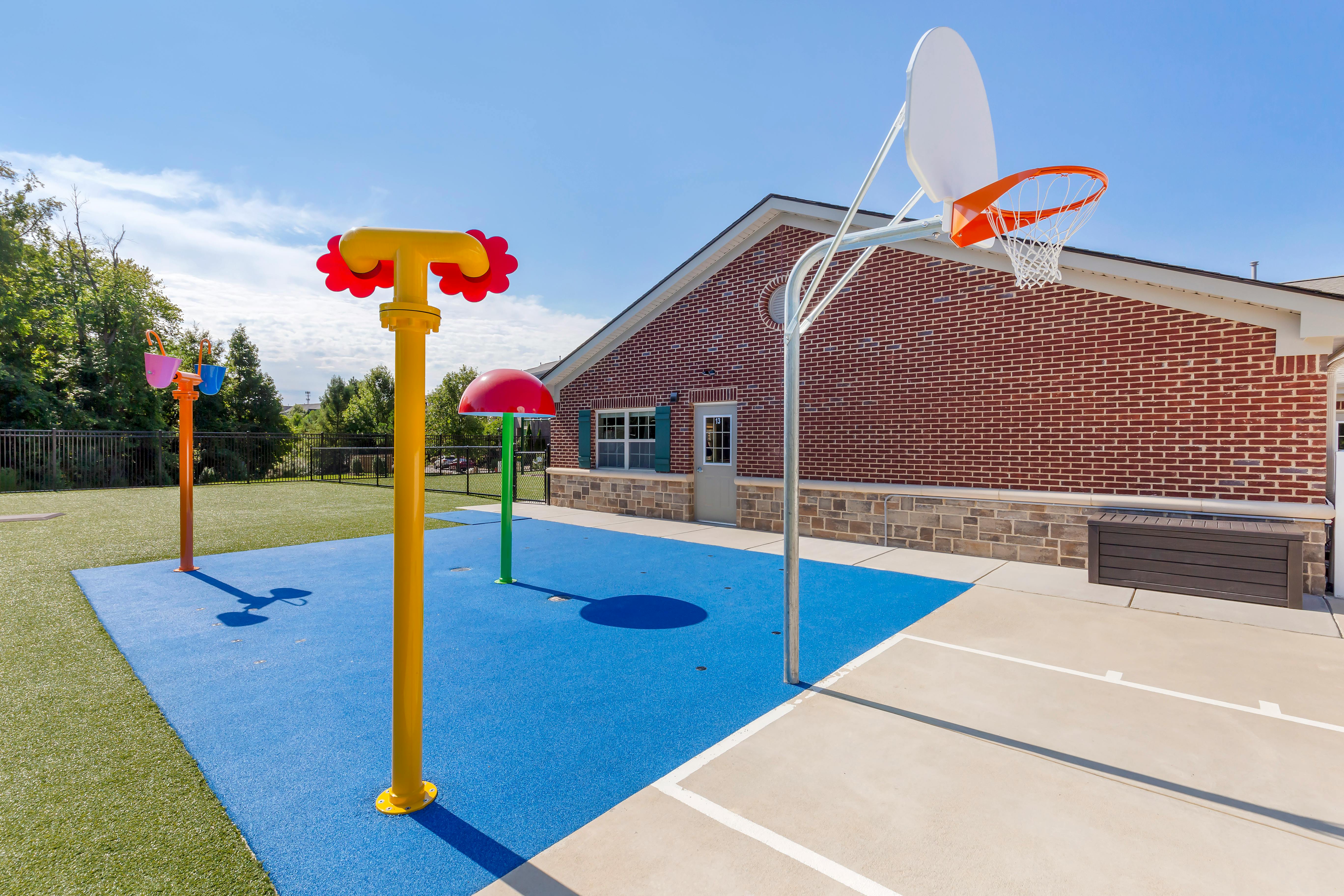 Outdoor play area with water features and a basketball hoop next to a brick building