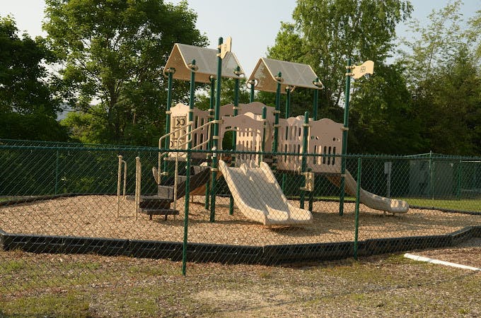 Empty playground with tan and green structure and two slides, surrounded by a fence