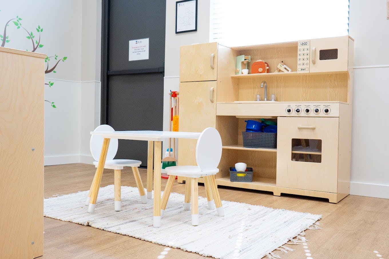 Wooden play kitchen set with a small table and two chairs in a playroom