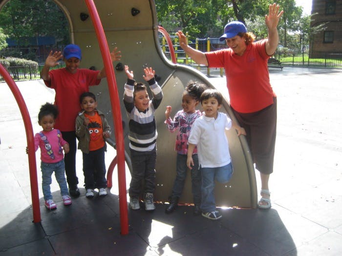 Two adults and five children on a playground structure with hands raised