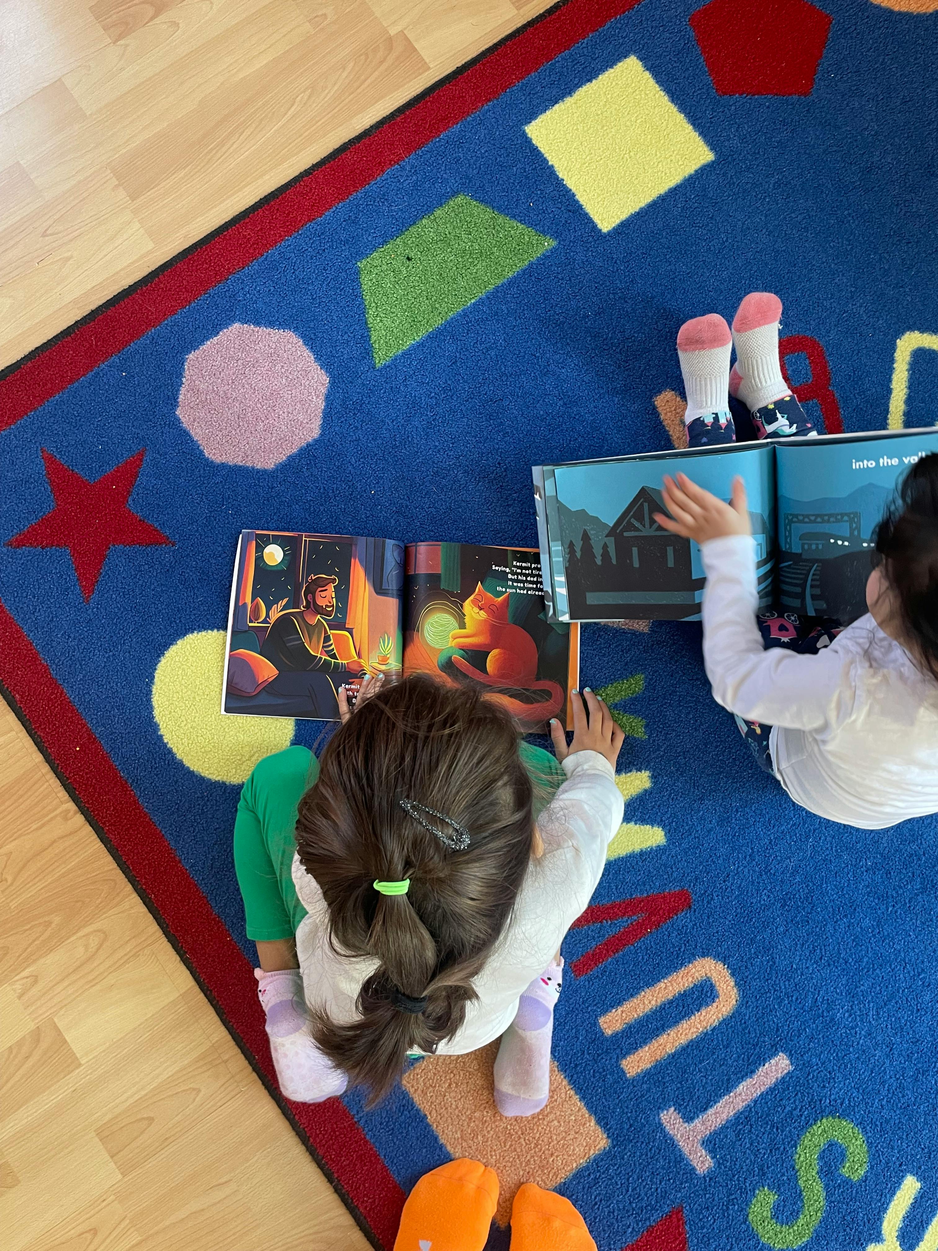 Two children sitting on a rug reading open books